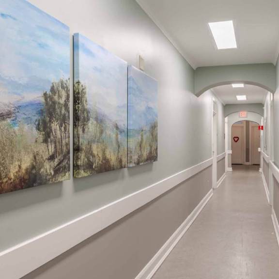 a hallway with a painting on the wall and a door at the end.