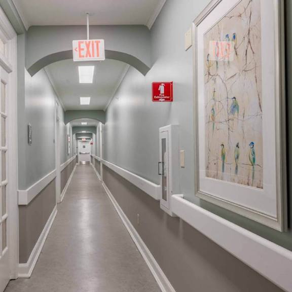 a long hallway with doors on the left and a red exit sign hanging from the ceiling.