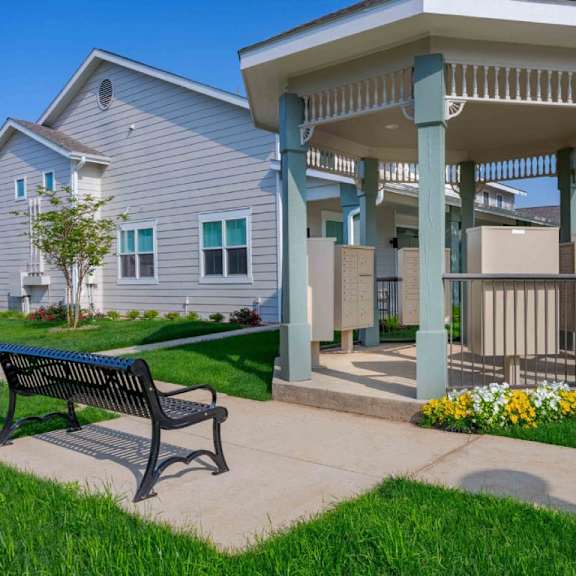 a bench is on a sidewalk in front of a house and a gazebo.