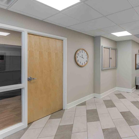 a hallway with a clock on the wall and a couch on the right side.