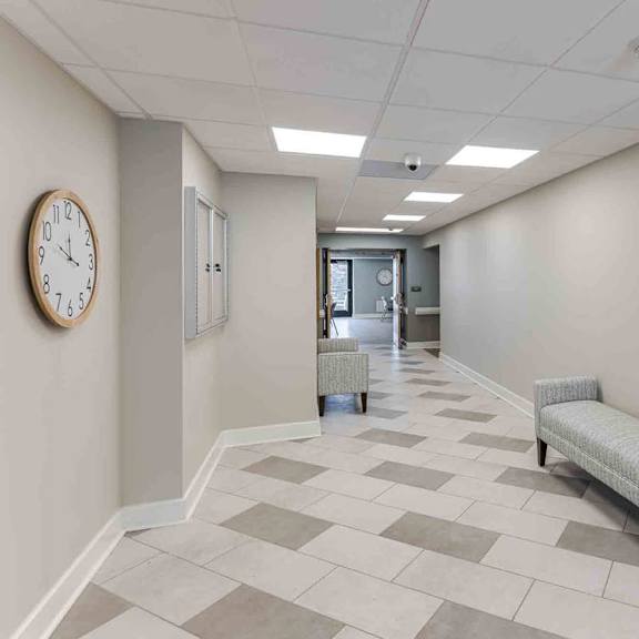 a hallway with a bench, a clock, and a whiteboard.
