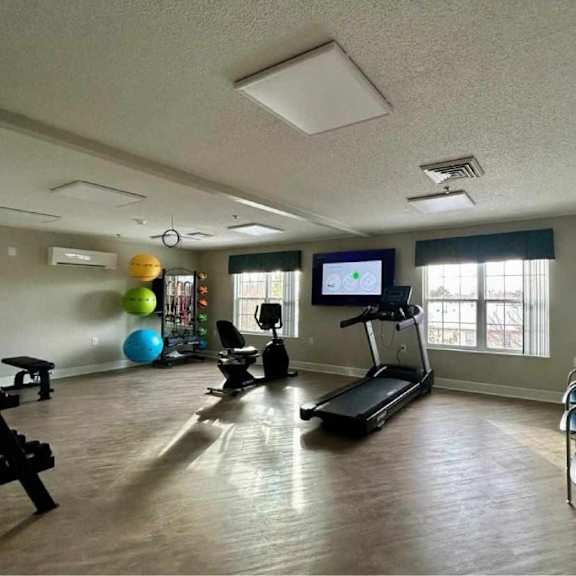 a spacious room with a treadmill, exercise balls, and a row of chairs.