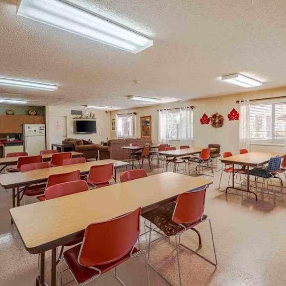 a room with tables and chairs and a kitchen area in the background.