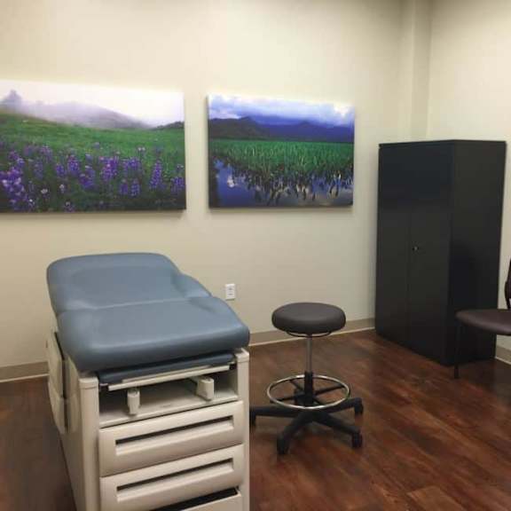 a medical examination room with a treatment bed, two chairs, and two paintings on the wall.