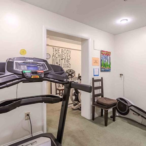 a gym room with a treadmill, a stationary bike, and a wall with a sign that says "the body achieves what the mind believes".
