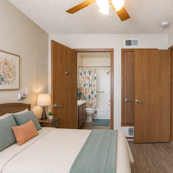 a bedroom with a bed, a lamp, a painting, and a ceiling fan.
