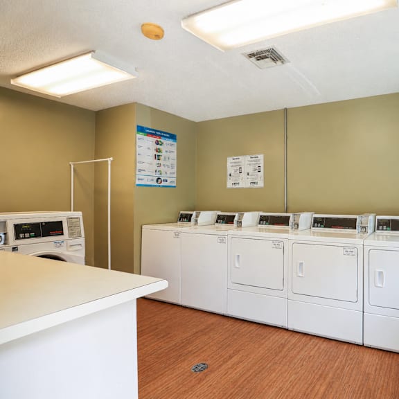 a laundry room with a white counter and three washing machines.