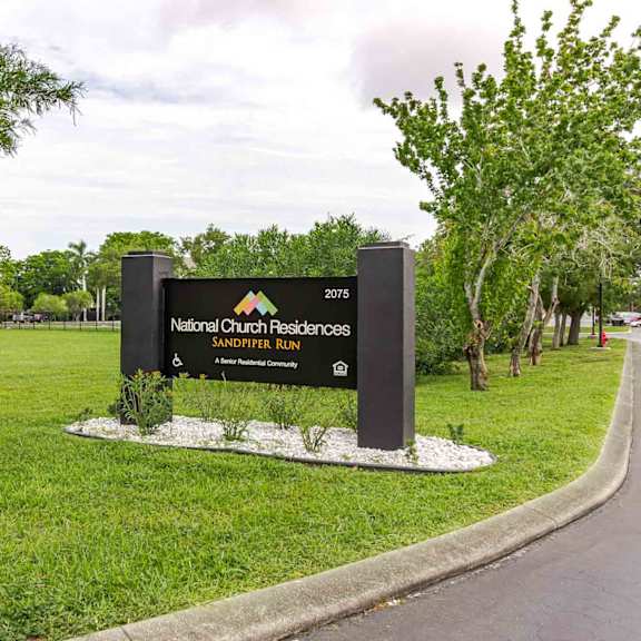 a sign for national church residences and sandpiper run stands in a grassy area.
