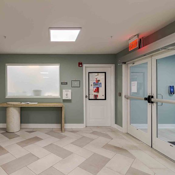 a hallway with a bench, a plant, and a door with a glass panel.