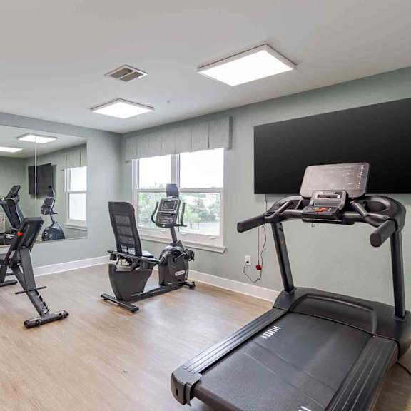 a spacious gym with treadmills, elliptical machines, and dumbbells.