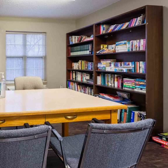 a room with a table, chairs, and bookshelves filled with books.