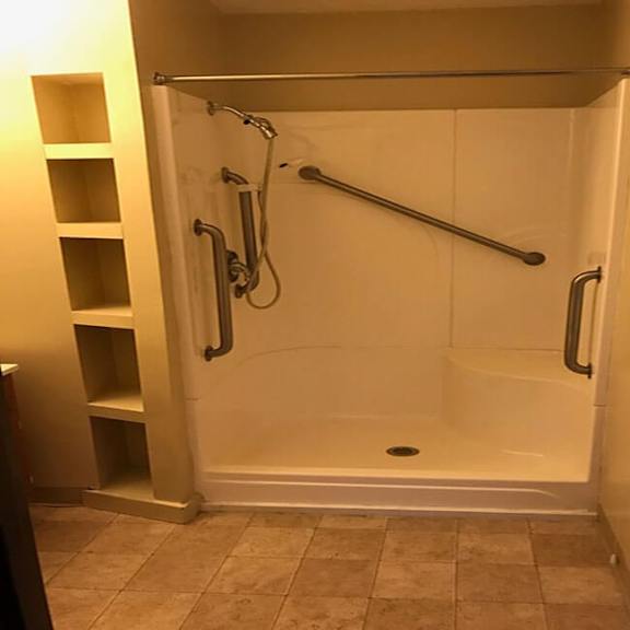 a white shower stall with a glass door and a silver grab bar.