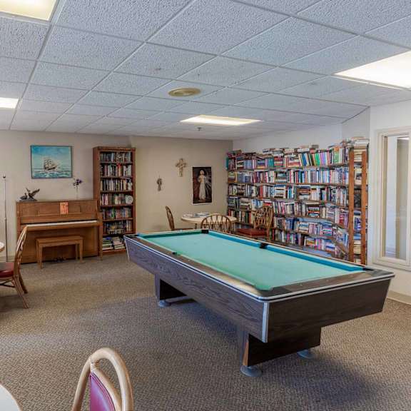 a room with a pool table, chairs, and a bookcase.