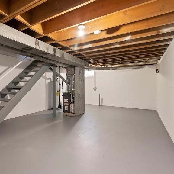a basement with stairs and a white wall and a ceiling with wooden beams