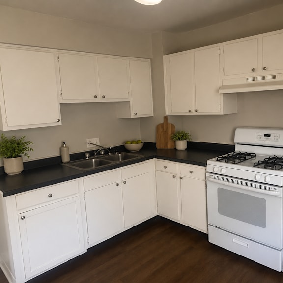 a white kitchen with black countertops and wooden floors.
