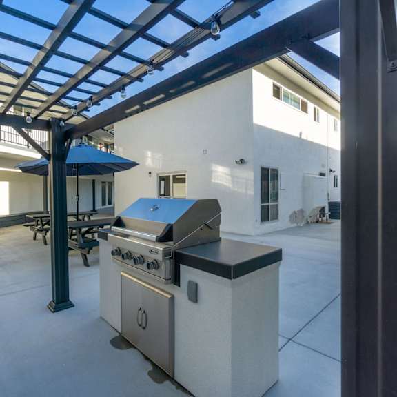 a modern outdoor kitchen area with a grill and a table. at torrance gateway apartments, torrance, 90501
