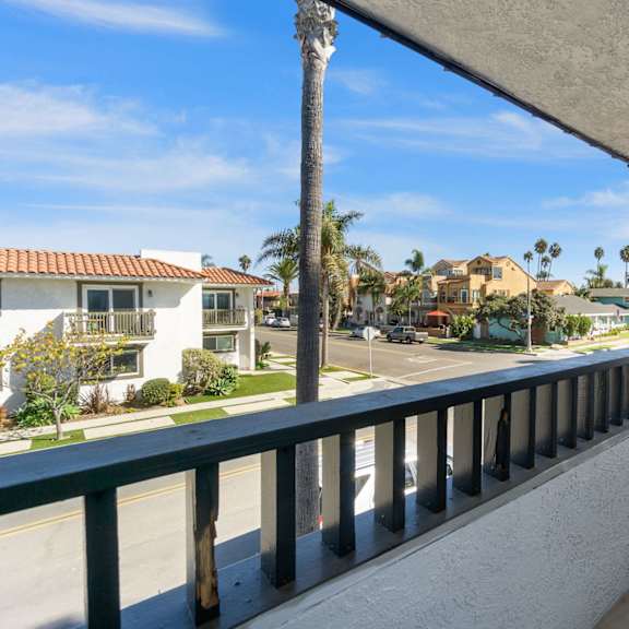 a balcony with a view of the street and palm trees at ocean breeze terrace apartment, huntington beach, 92648