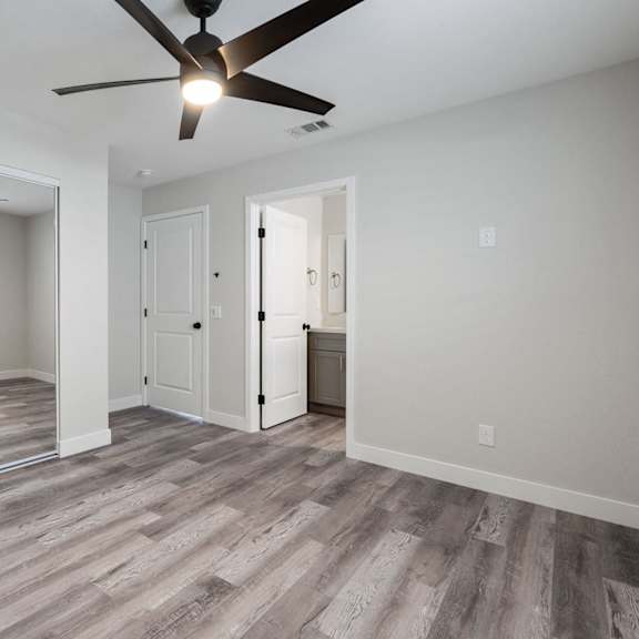 an empty living room with a ceiling fan and a door to a bathroom