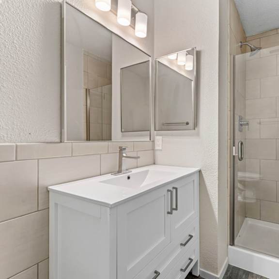 a white bathroom with a sink, mirror, and shower.