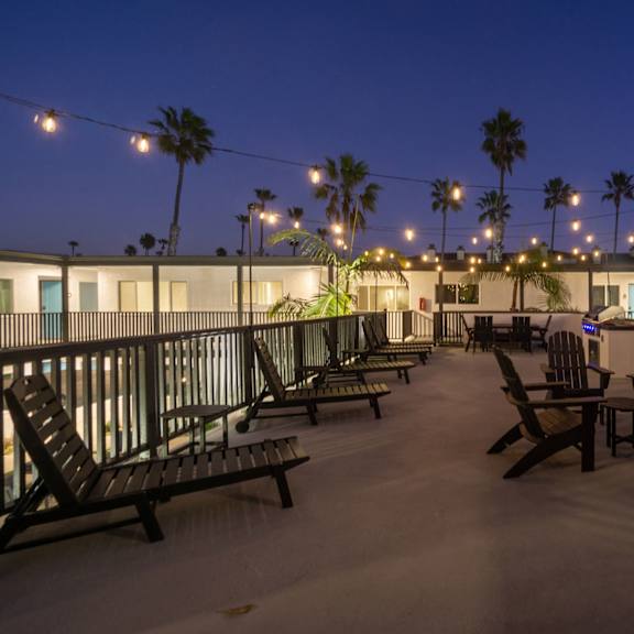 a patio with chairs and a table is lit by string lights at ocean breeze terrace apartment, huntington beach, ca
