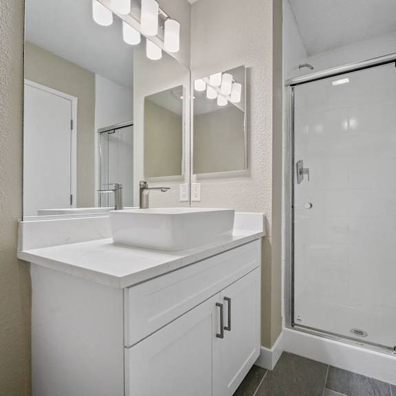 a white bathroom with a sink, mirror, and shower at tamarack sands apartment homes, california