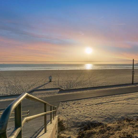 a sunset view of a beach with a metal railing in the foreground at ocean breeze terrace apartment, huntington beach