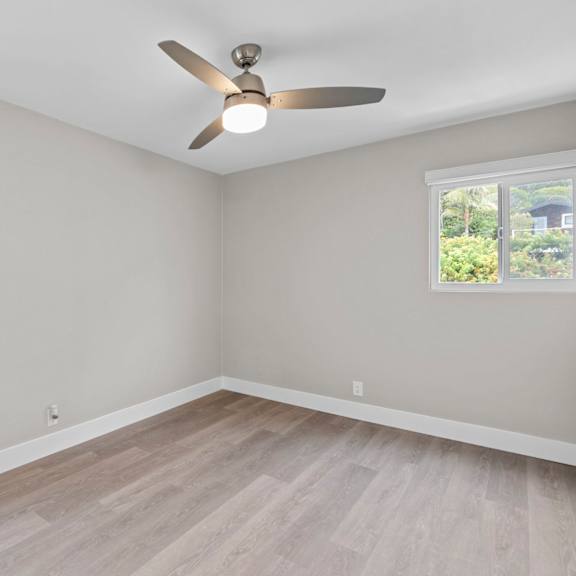a room with a ceiling fan and two windows.