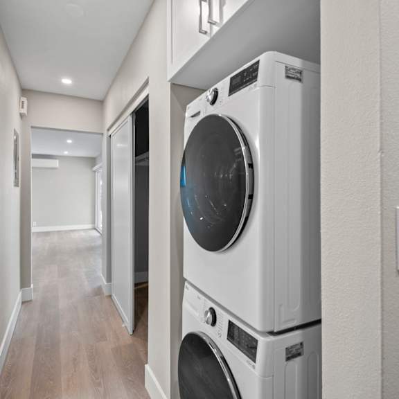 a white washing machine is stacked on top of another white washing machine in a narrow hallway.