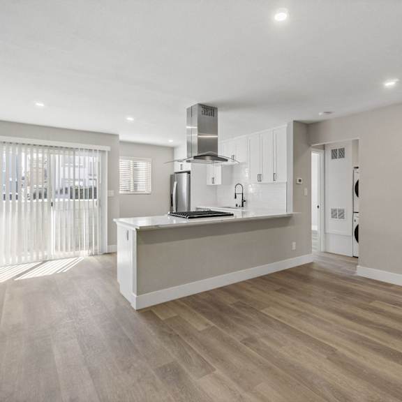 a renovated living room and kitchen with white walls and wood floors at ocean breeze terrace apartment, huntington beach
