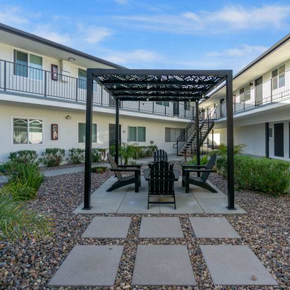 a patio with a table and chairs is surrounded by white buildings. at torrance gateway apartments, torrance, 90501