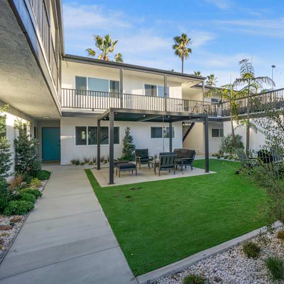 a patio with a table and chairs is surrounded by a green lawn. at ocean breeze terrace apartment, huntington beach, 92648