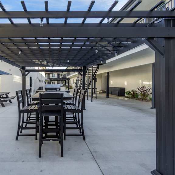 a patio with a table and chairs under a pergola. at torrance gateway apartments, california