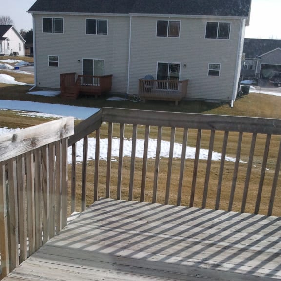 a deck with a wooden railing and a house in the background