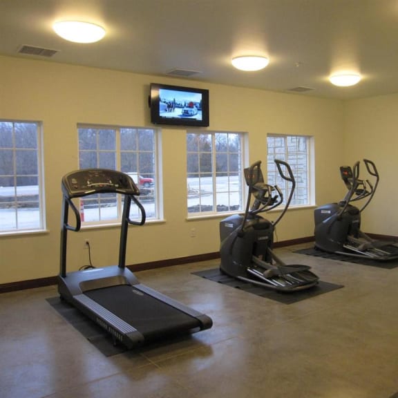a gym with three treadmills and a tv