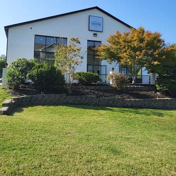 the front of a white building with a lawn and trees at schaefer ridge apartments, branson , mo