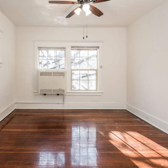 a room with a ceiling fan and two windows.