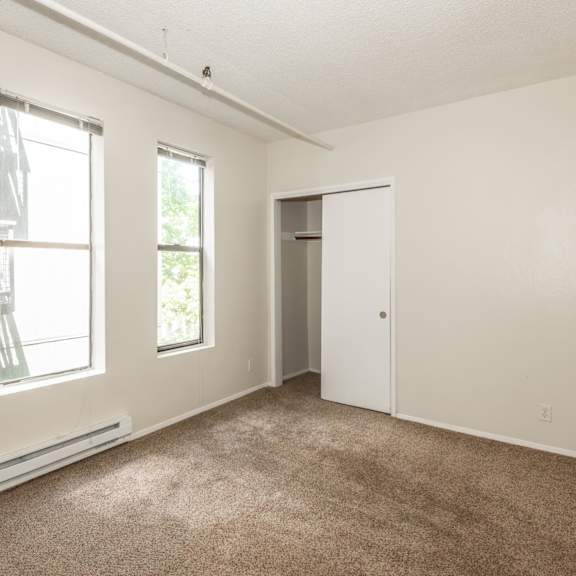 a room with a carpeted floor, two windows, and a door.