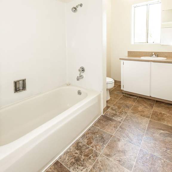 a white bathroom with a tiled floor and a bathtub.