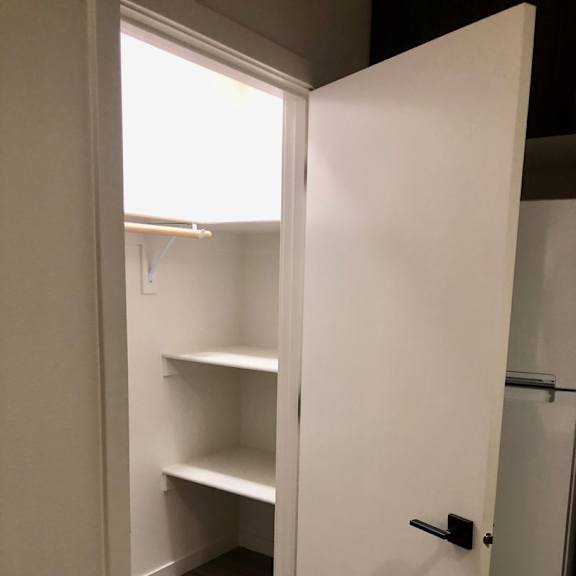 a white closet with a black handle and a shelf.