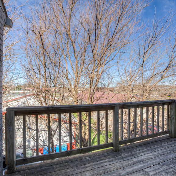 a wooden deck with a brick wall on the left side and leafless trees in the background.