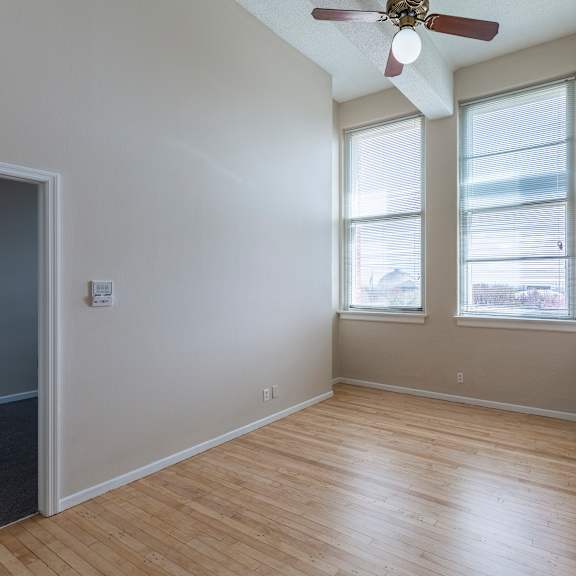 a room with a ceiling fan and two windows.