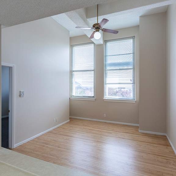 a room with a ceiling fan and two windows.