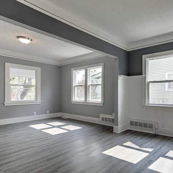 a room with grey walls and wooden flooring with a window on the left.