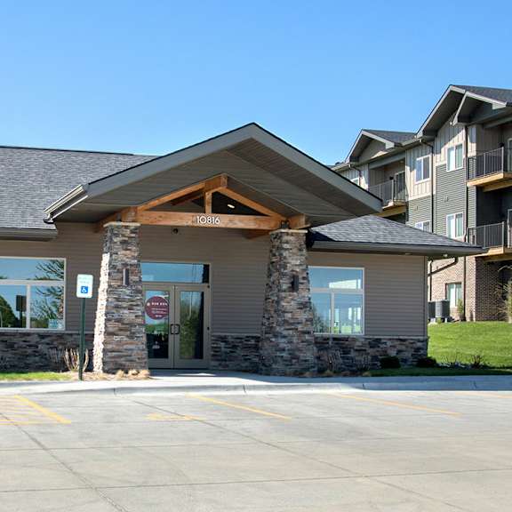 a building with a stone pillar entrance and a parking lot in front.
