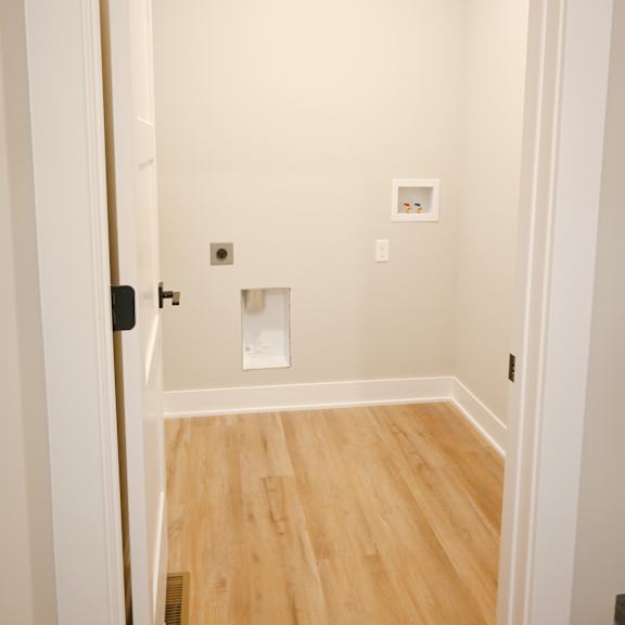 a white door is open to a room with wood flooring.