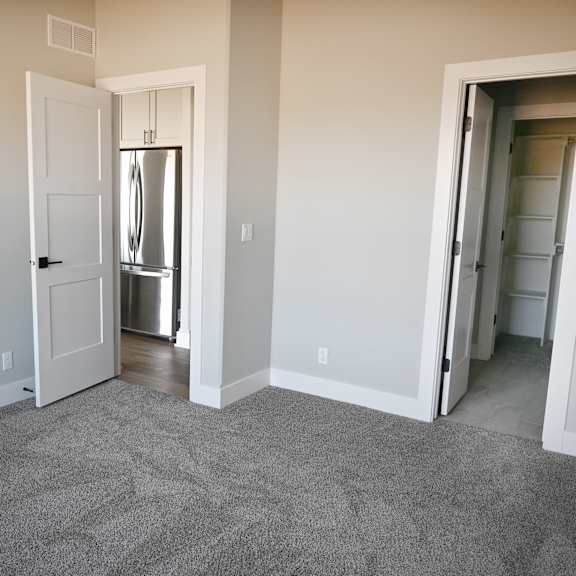 a room with a carpeted floor and a white door leading to a kitchen.