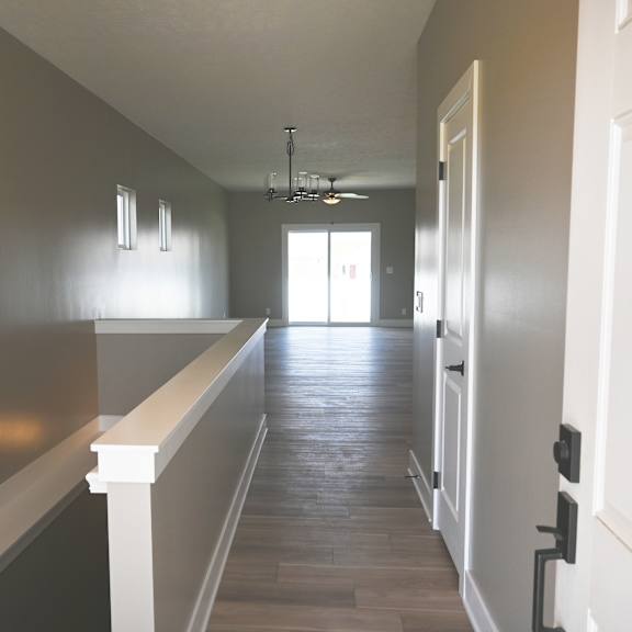 a long hallway with a white railing on the left side and a door on the right.