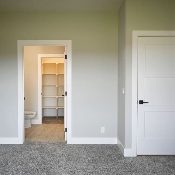 a room with a white door and a hallway with a toilet and a shelf.