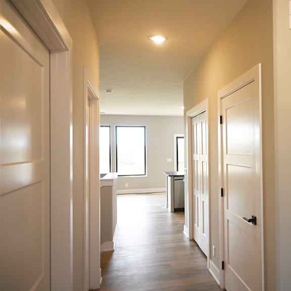 a long hallway with white doors and a window.