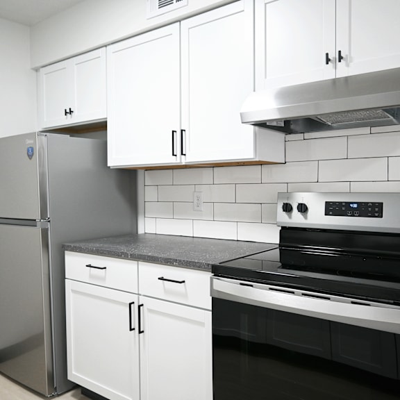 a kitchen with a stainless steel refrigerator, white cabinets, and a black stove top oven.